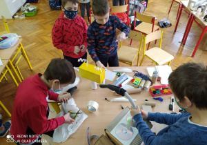 Czterech chłopców w trakcie składania robota z materiałów papierniczych.