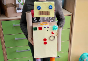 Uczeń na tle szafek prezentuje dużego robota.