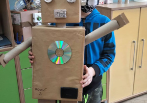 Uczeń na tle szafek prezentuje dużego robota.