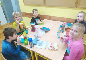 Grupa uczniów spożywa śniadanie przy wspólnym stole