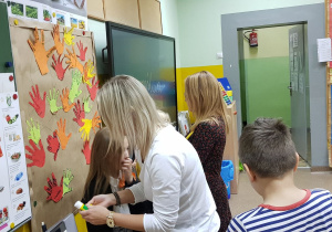 Rodzice przyklejają do planszy papierowe dłonie