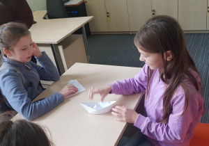 Dziewczynki robią łódki z papieru.