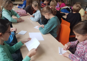 Uczniowie składają łódki z papieru.