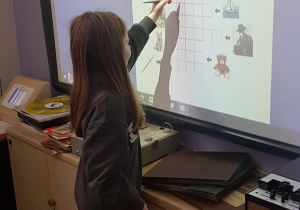Dziewczynka uzupełnia krzyżówkę na tablicy multimedialnej.