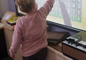 Dziewczynka uzupełnia krzyżówkę na tablicy multimedialnej.