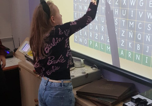 Dziewczynka uzupełnia krzyżówkę na tablicy multimedialnej.