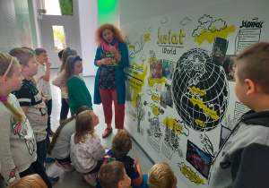 Grupa uczniów w kręgu z prowadzącą zajęcia przed tablicą "Świat"