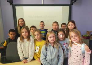 Grupa uczniów z prowadzącą zajęcia przed tablicą multimedialną