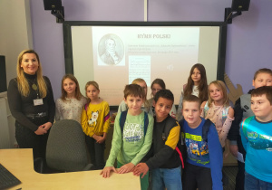 Grupa uczniów z prowadzącą zajęcia przed tablicą multimedialną