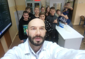 Grupa uczniów i nauczyciel chemii przy stole roboczym w pracowni chemicznej