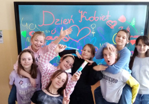 Grupa dziewcząt na tle tablicy multimedialnej z wpisami okolicznościowymi