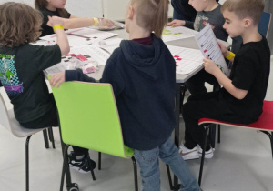 Uczniowie siedzą przy stoliku. Instruktorka tłumaczy zadanie.