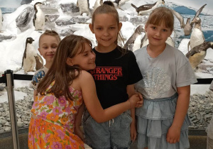 Trzy dziewczynki i chłopiec na tle wystawy pingwinów.