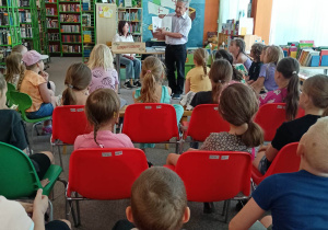 Poeta prezentuje książkę. Uczniowie siedzą na krzesłach.