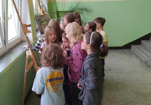 Uczniowie stoją przy sztalugach ze zdjęciami nauczycieli