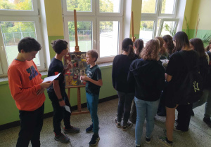 Uczniowie klas starszych przed sztalugami ze zdjęciami nauczycieli
