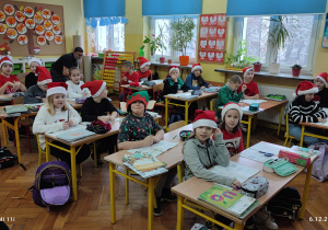 Uczniowie w ławkach w czapkach mikołajowych