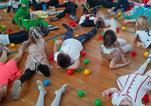 Uczniowie leżą na podłodze, wokół kolorowe kulki.