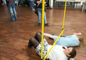 Dziewczynki usiłują przecisnąć się pod nisko osadzoną poprzeczką.