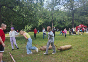 Zosia ciągnie drewniany klocek, a Marysia próbuje ją dogonić.