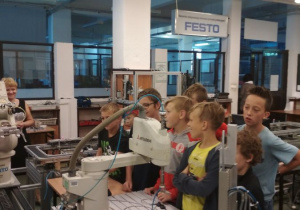 Uczniowie obserwują pracę robotów przemysłowych linii produkcyjnej.