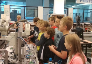 Uczniowie obserwują pracę robotów przemysłowych linii produkcyjnej.