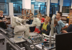 Uczniowie obserwują pracę robotów przemysłowych linii produkcyjnej.