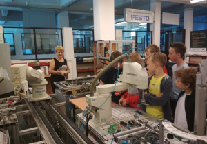 Uczniowie obserwują pracę robotów przemysłowych linii produkcyjnej.