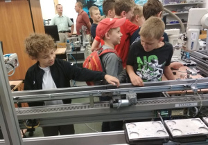 Uczniowie obserwują pracę robotów przemysłowych linii produkcyjnej.