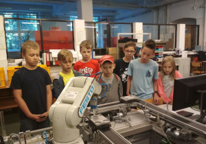 Uczniowie obserwują pracę robotów przemysłowych linii produkcyjnej.