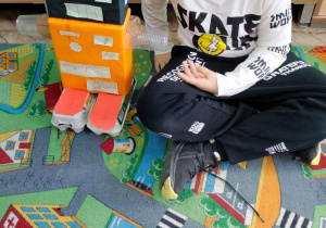 Uczeń siedzi na dywanie obok swojego robota.