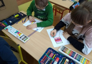 Dwoje uczniów przy ławce kolorują papierowe skarpety