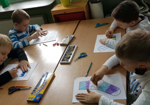 Czterej uczniowie przy stolikach podczas kolorowania papierowych skarpet