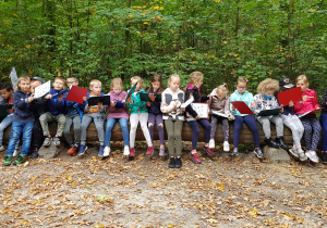 Grupa dzieci siedzi na powalonym pniu