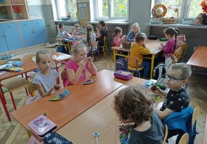 Uczniowie spożywają ciasto siedząc przy stolikach