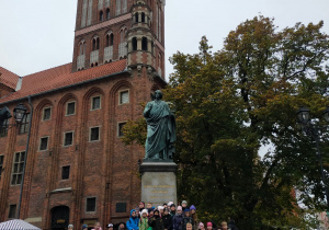 Grupa dzieci przed pomnikiem Mikołaja Kopernika.