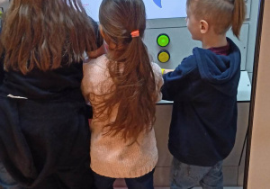 Troje uczniów bawi się przy ekranie interaktywnym.