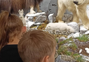 Troje uczniów stoi przed niedźwiedziem polarnym.