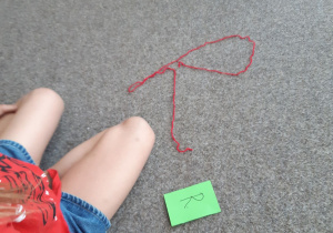 Litera R ułożona z czerwonej włóczki na dywanie.