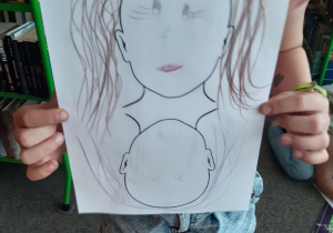 Dziewczynka prezentuje rysunek - portret dziewczynki.