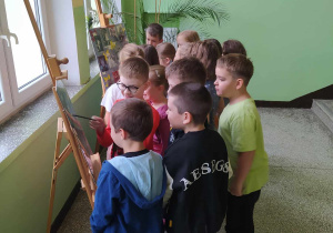 Grupa uczniów przy sztalugach ze zdjęciami nauczycieli