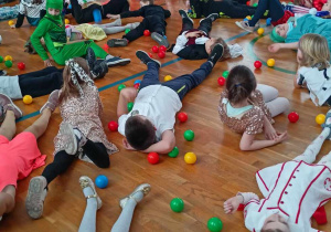 Uczniowie leżą na podłodze, wokół kolorowe kulki.