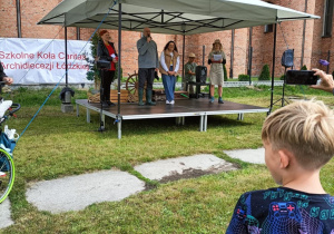 Rozpoczęcie pikniku. Na scenie prowadzący, a w tle kościół Przenajświętszej Trójcy