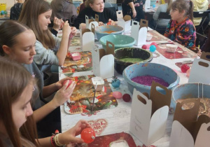 Uczniowie zgromadzeni wokół stołu z brokatem i ozdobami do tworzenia bombek