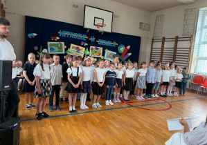 Uczniowie klas drugich stoją i śpiewają.