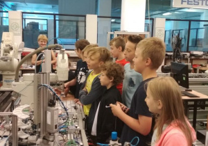 Uczniowie obserwują pracę robotów przemysłowych linii produkcyjnej.