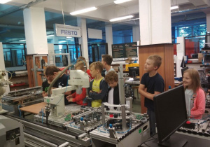 Uczniowie obserwują pracę robotów przemysłowych linii produkcyjnej.