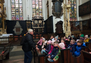 Dzieci słuchają w kościele wypowiedzi przewodnika.